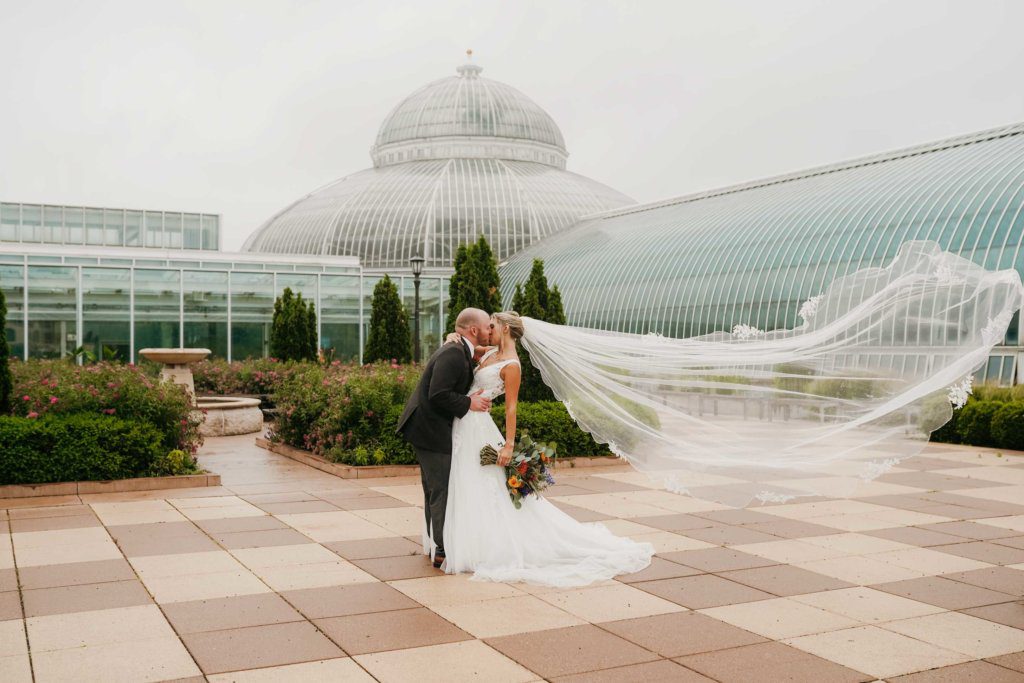 Bride and groom wedding photography of them kissing in front of their wedding venue at Como Park Conservatory in Saint Paul Minnesota 